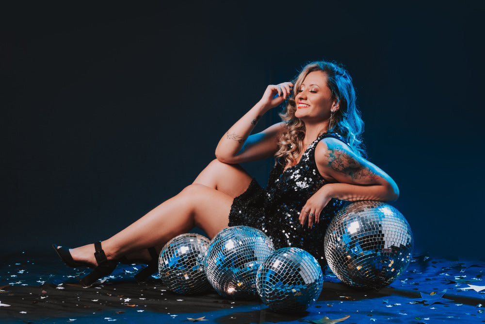 Woman in a gleam disco party dress sitting around silver disco balls